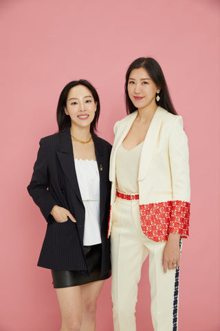 The founders of Antevorta, Sara Jane Ho and Annie Ho, standing against a pink background.
