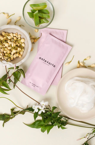 The Intimate wipe set against a pale yellow background. The pink wipes are surrounded by dried flower bugs, lush vines, and fluffy cotton.